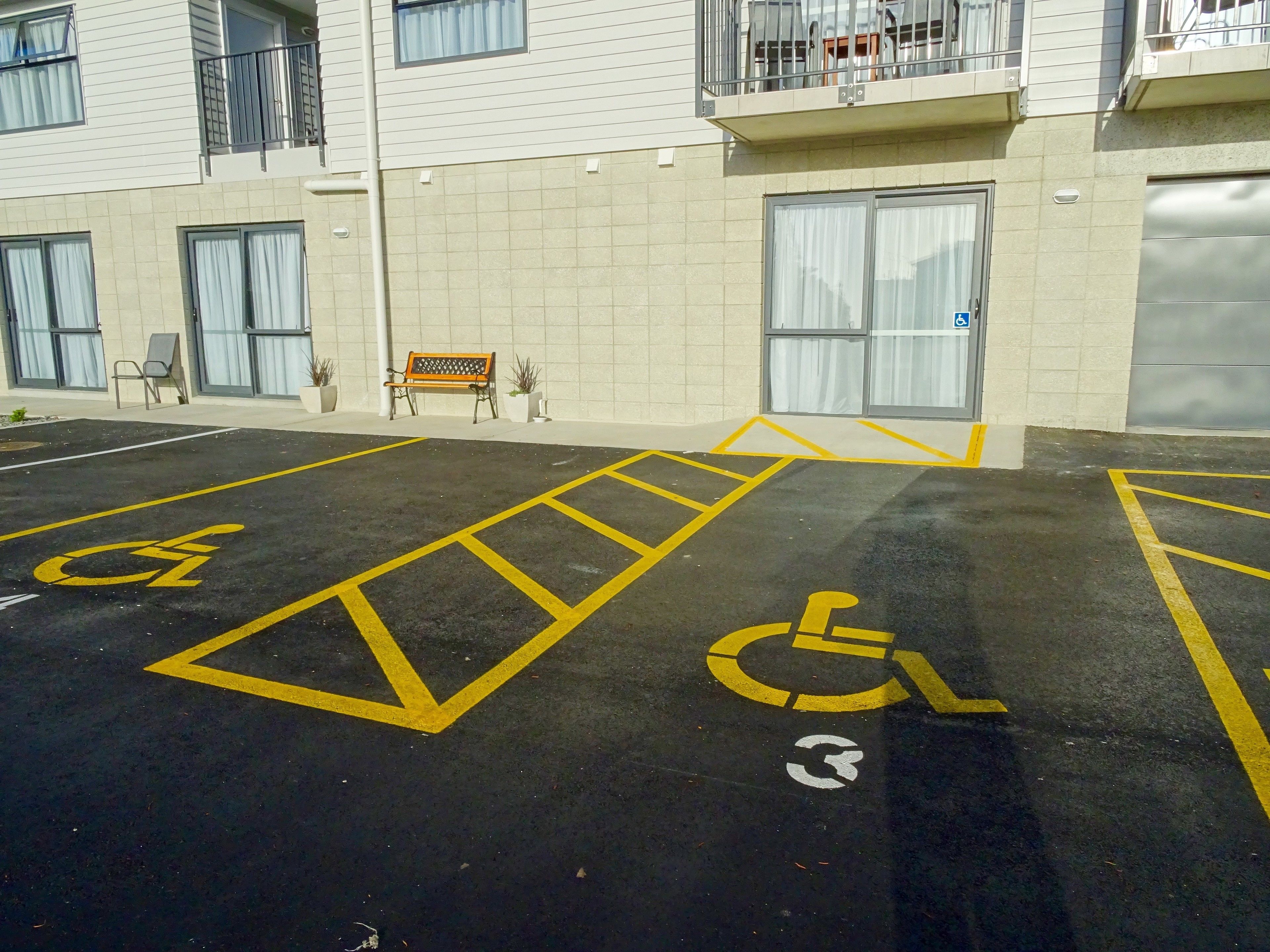 A parking lot with handicapped parking spaces, a bench, and a building with a balcony.