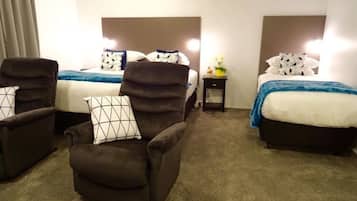 Quarto de hotel com duas camas, um sofá e uma mesa de cabeceira com abajur.