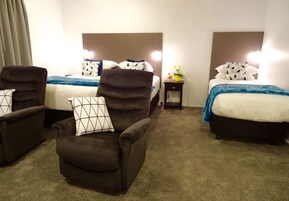 Quarto de hotel com duas camas, um sofá e uma mesa de cabeceira com abajur.