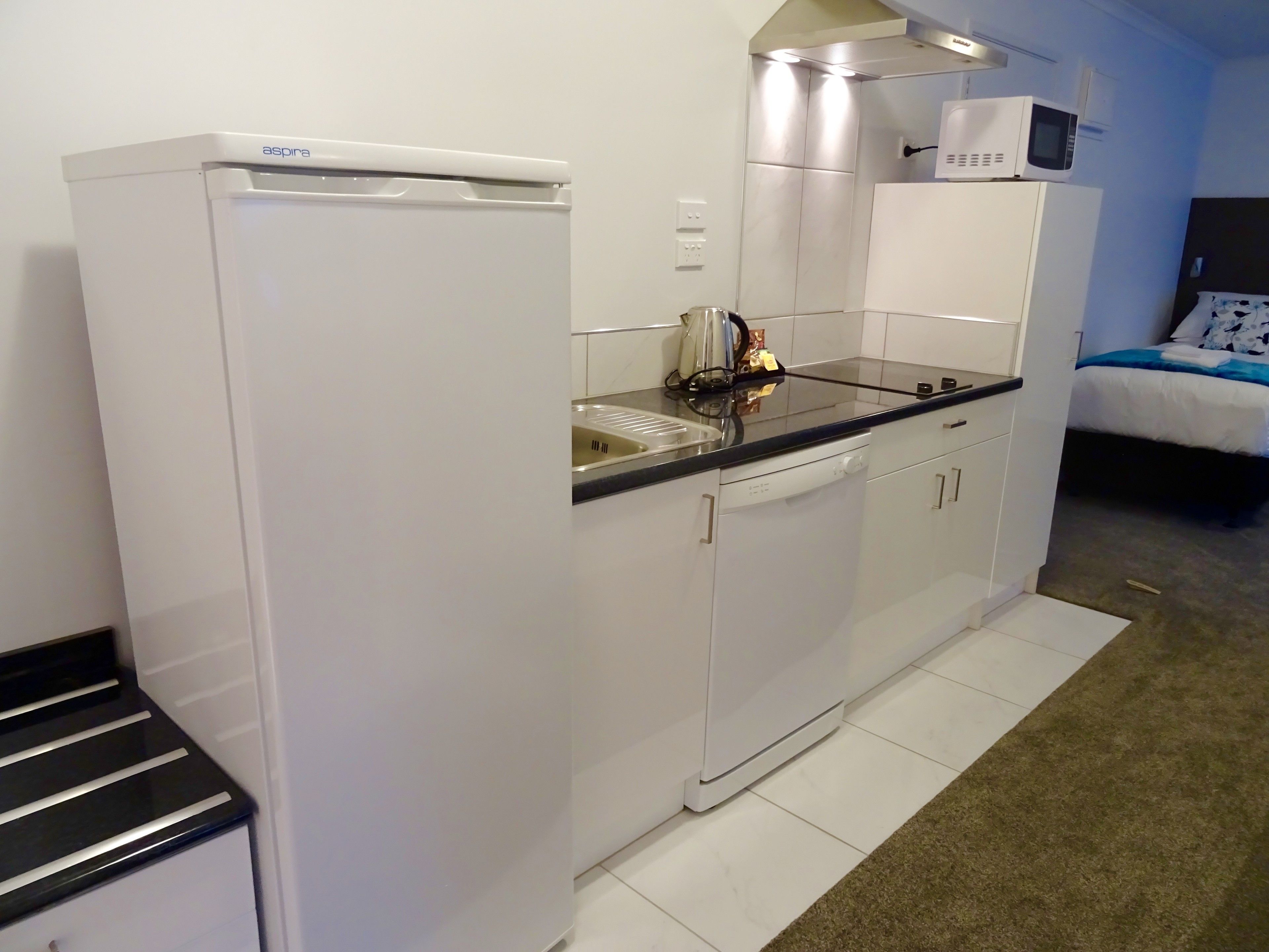 A compact kitchenette with a white refrigerator, a microwave, and a dishwasher.