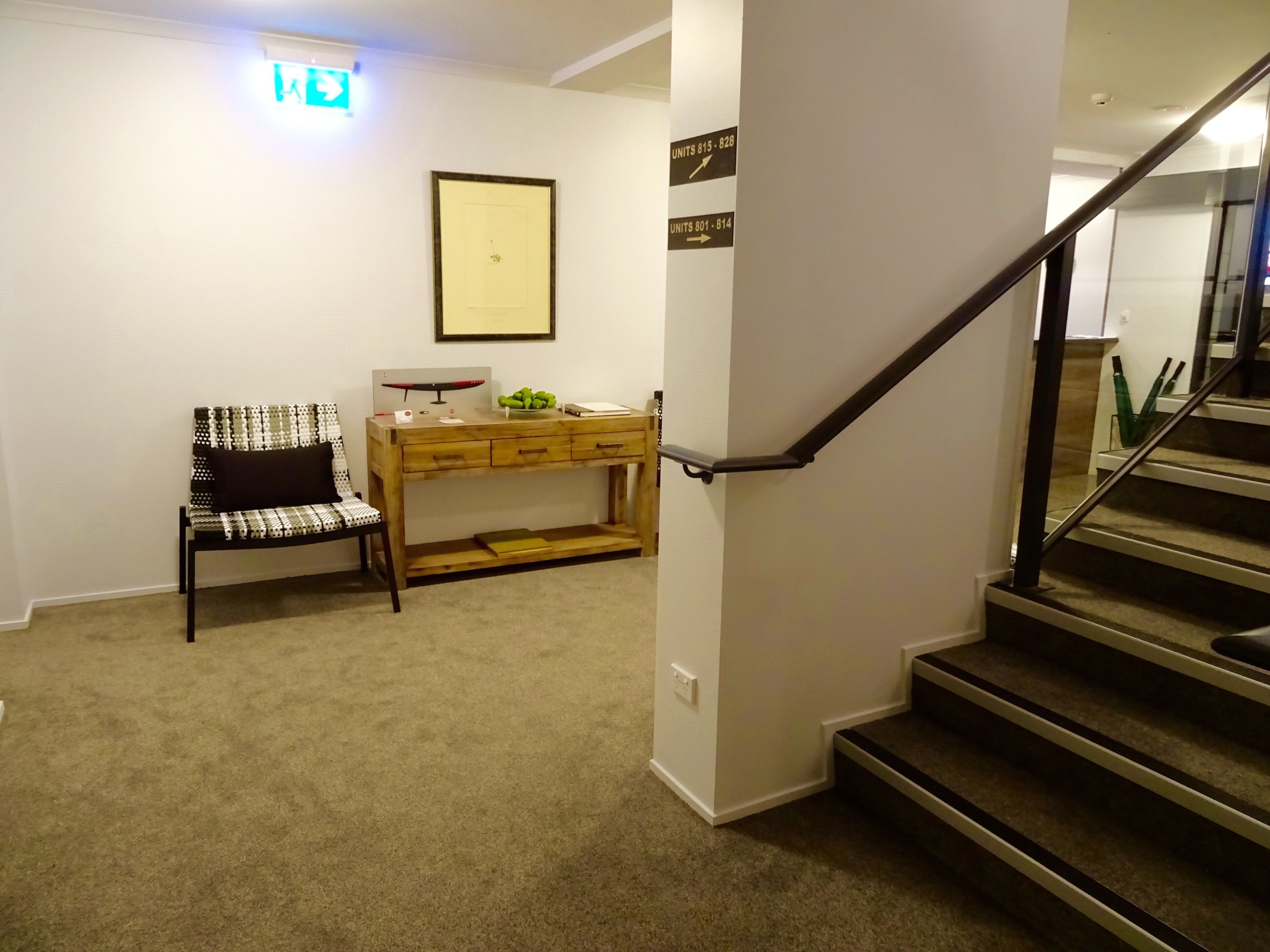 A carpeted hallway with a wooden desk, a chair, and a staircase.