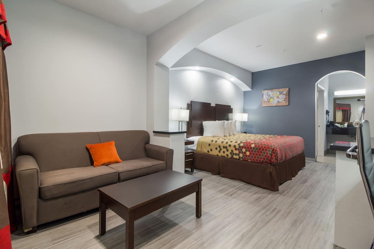 A hotel room with a sofa, a bed with a patterned bedspread, a small table, and a mirror.