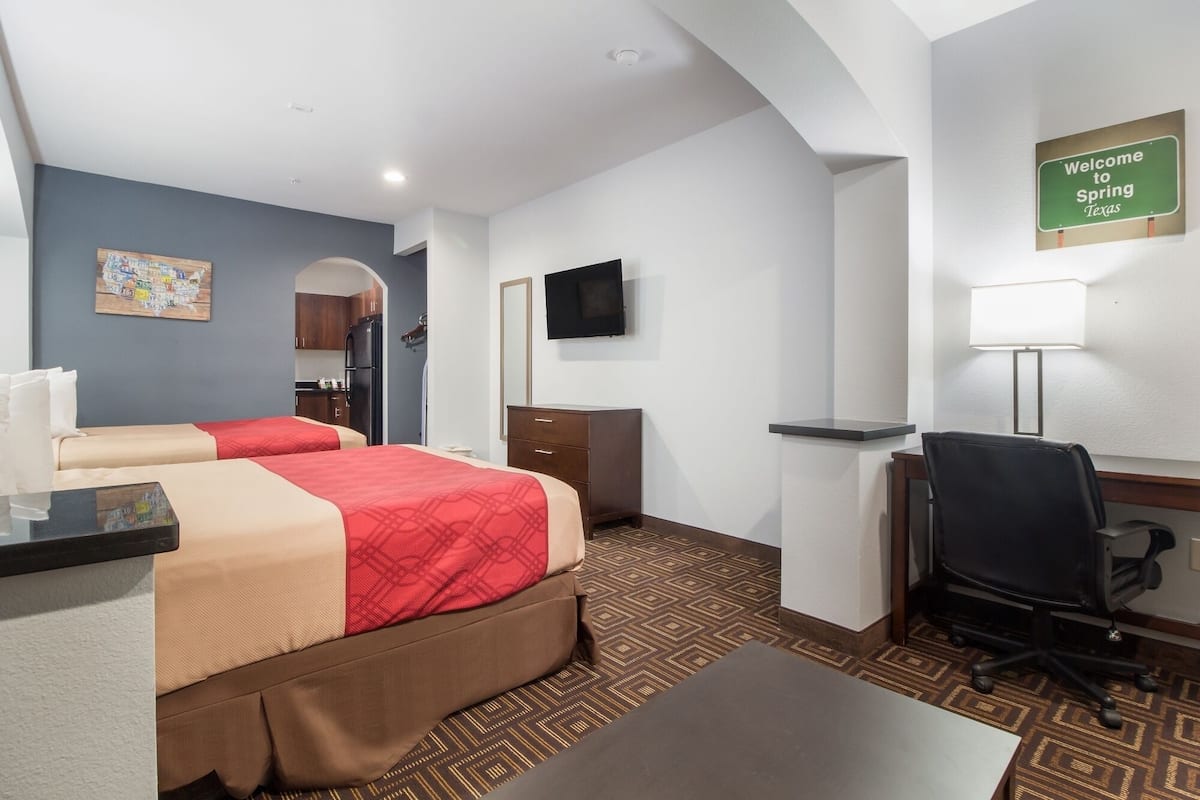 A hotel room with two beds, a desk, a chair, a TV, and a sign reading "Welcome to Spring Texas".