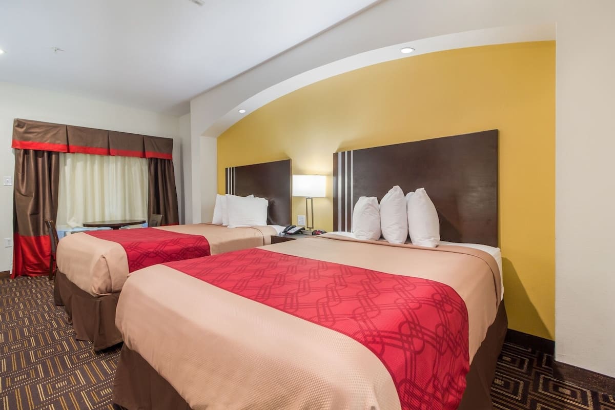 A hotel room with two beds, a desk, and a lamp.