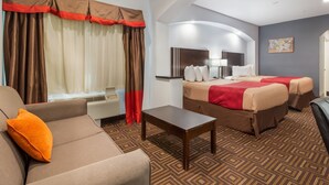 A hotel room with a sofa, two beds, a desk, and a large window with curtains. - Scottish Inns and Suites Spring, TX (Spring)