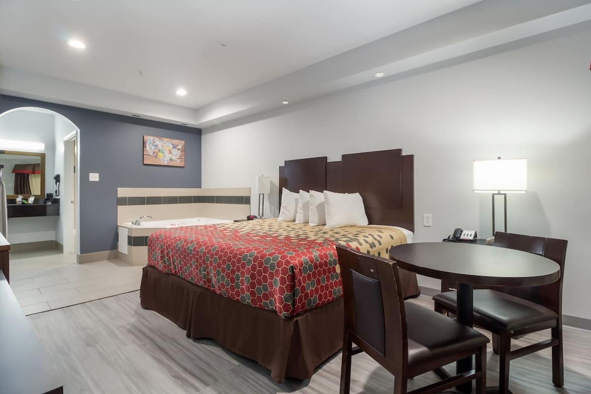 A hotel room with a bed, a desk, and a chair. There is a lamp on the desk and a phone on the desk.