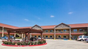 A hotel with a covered outdoor seating area, a fire lane, and a parking lot. - Scottish Inns and Suites Spring, TX (Spring)