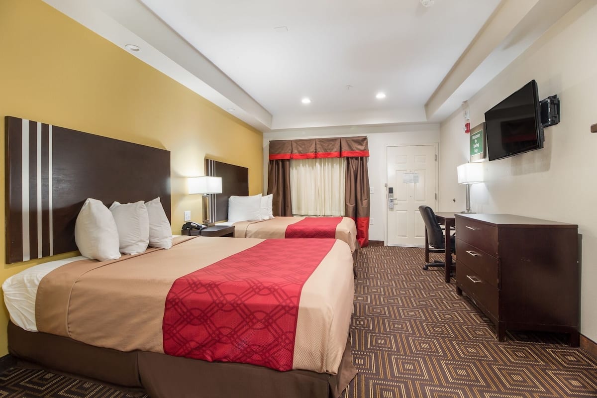 A hotel room with two beds, a desk, a chair, a television, and a wardrobe.