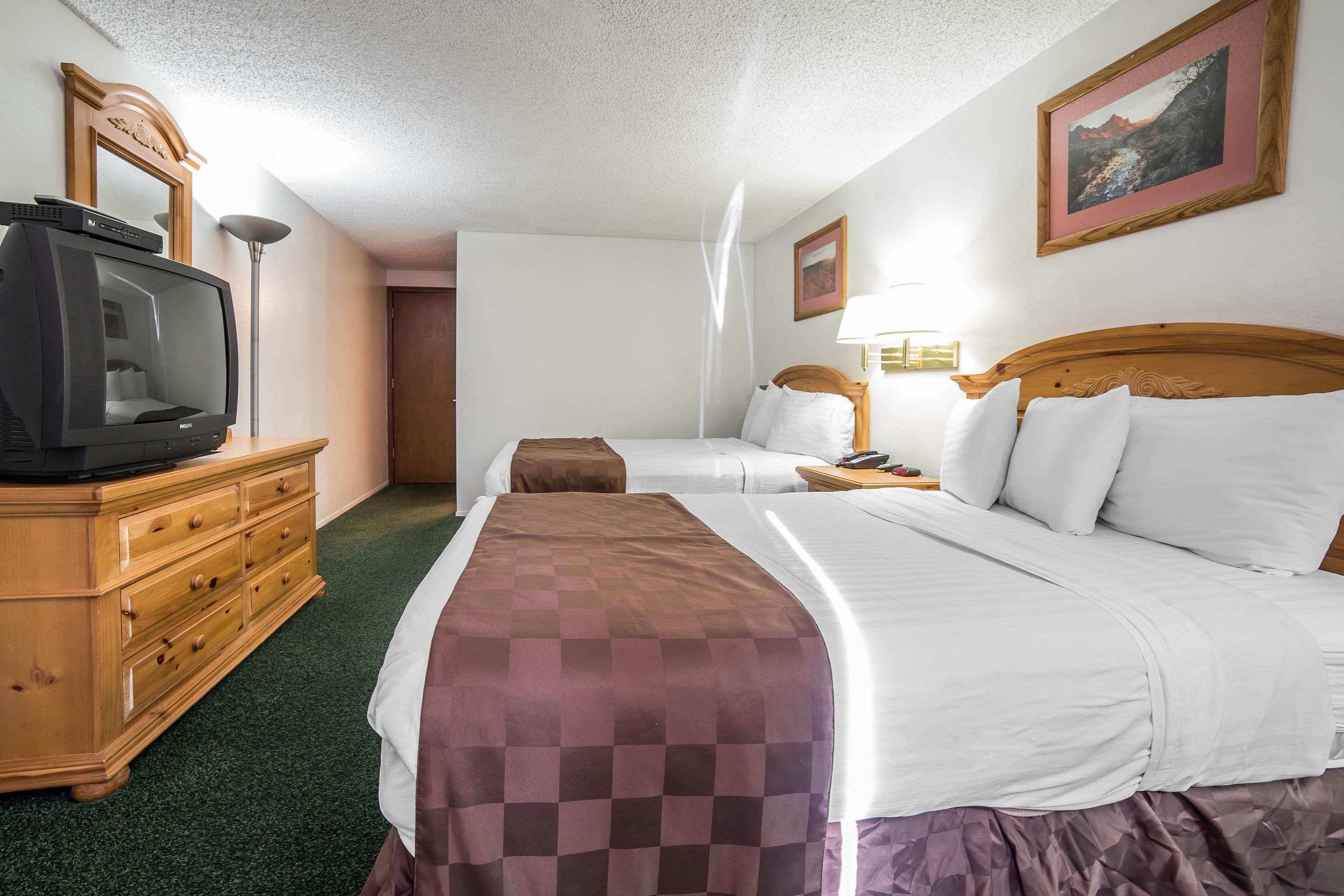 A hotel room with two beds, a wooden dresser, a television, and a framed picture on the wall.