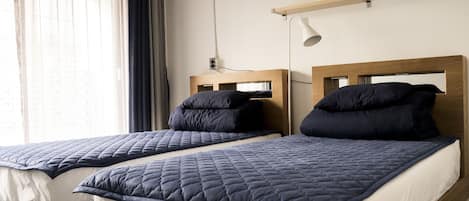 Dos camas individuales con cabeceros de madera y ropa de cama azul oscuro, una mesita de noche y una lámpara de pared.