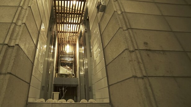 Un couloir étroit, carrelé, avec un plafond en lattes de bois et une rambarde métallique d’un côté.