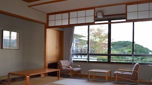 A traditional Japanese room with tatami flooring, a low table, two chairs, and a view of a hillside. - Hamayu Kuroshio Sanso (Shirahama)