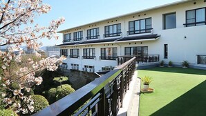 A modern building with multiple windows and balconies, a green lawn, and a tree with pink blossoms. - Hamayu Kuroshio Sanso (Shirahama)