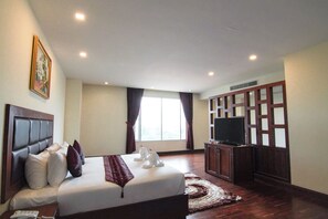 A hotel room with a large bed, a television, and a window with curtains.