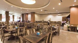 A large dining area with multiple tables and chairs, a central serving station, and a few people in the background.