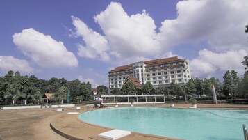 Un hotel con piscina, rodeado de árboles y un edificio grande al fondo.