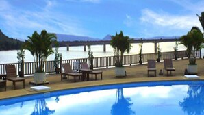 A pool area with lounge chairs and potted plants, overlooking a body of water and a distant mountain range. - Arawan Riverside Hotel (Pakse)