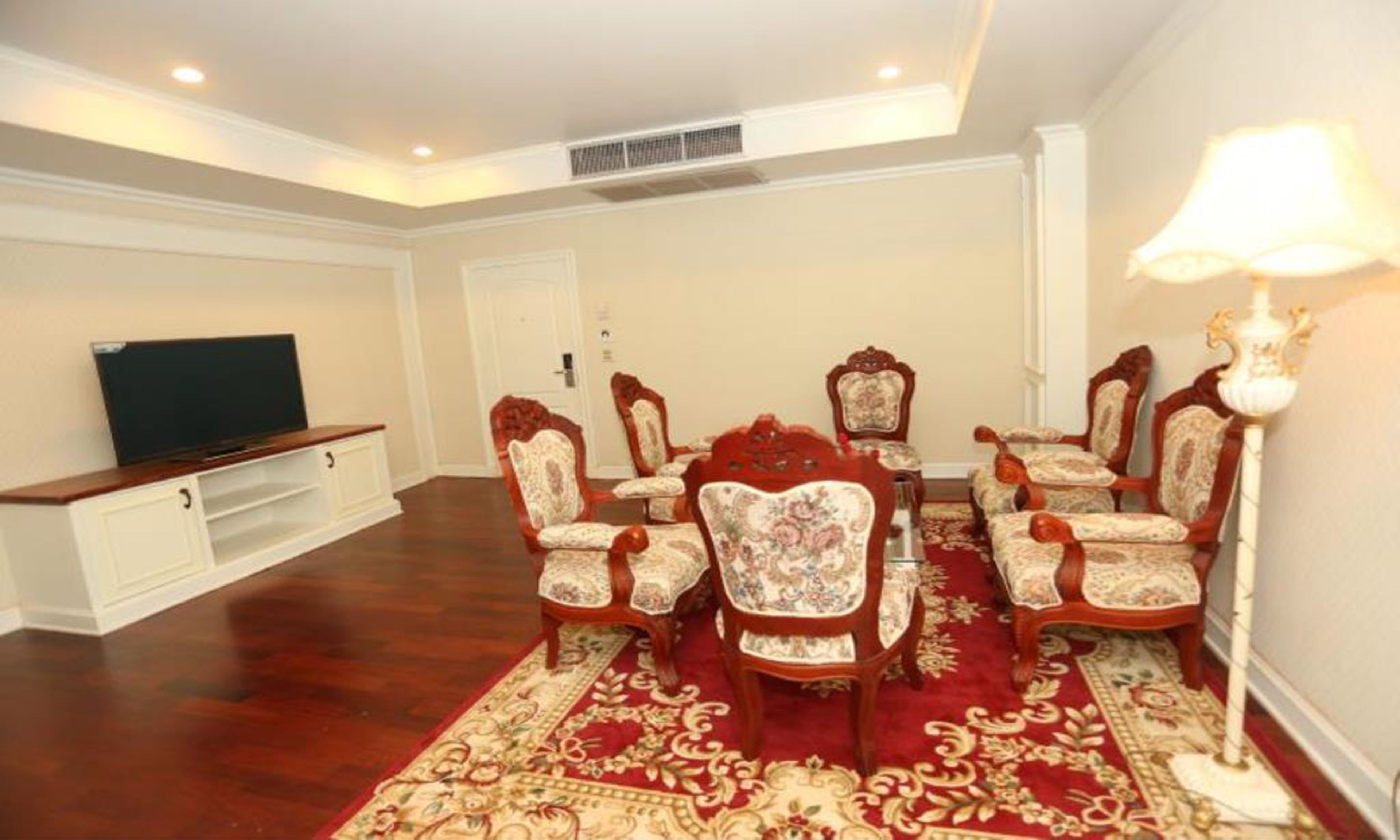 A dining room with a red carpet, wooden chairs, a television, and a white cabinet.