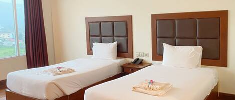 A hotel room with two single beds, wooden headboards, white bedding, a bedside telephone, and a window with curtains.