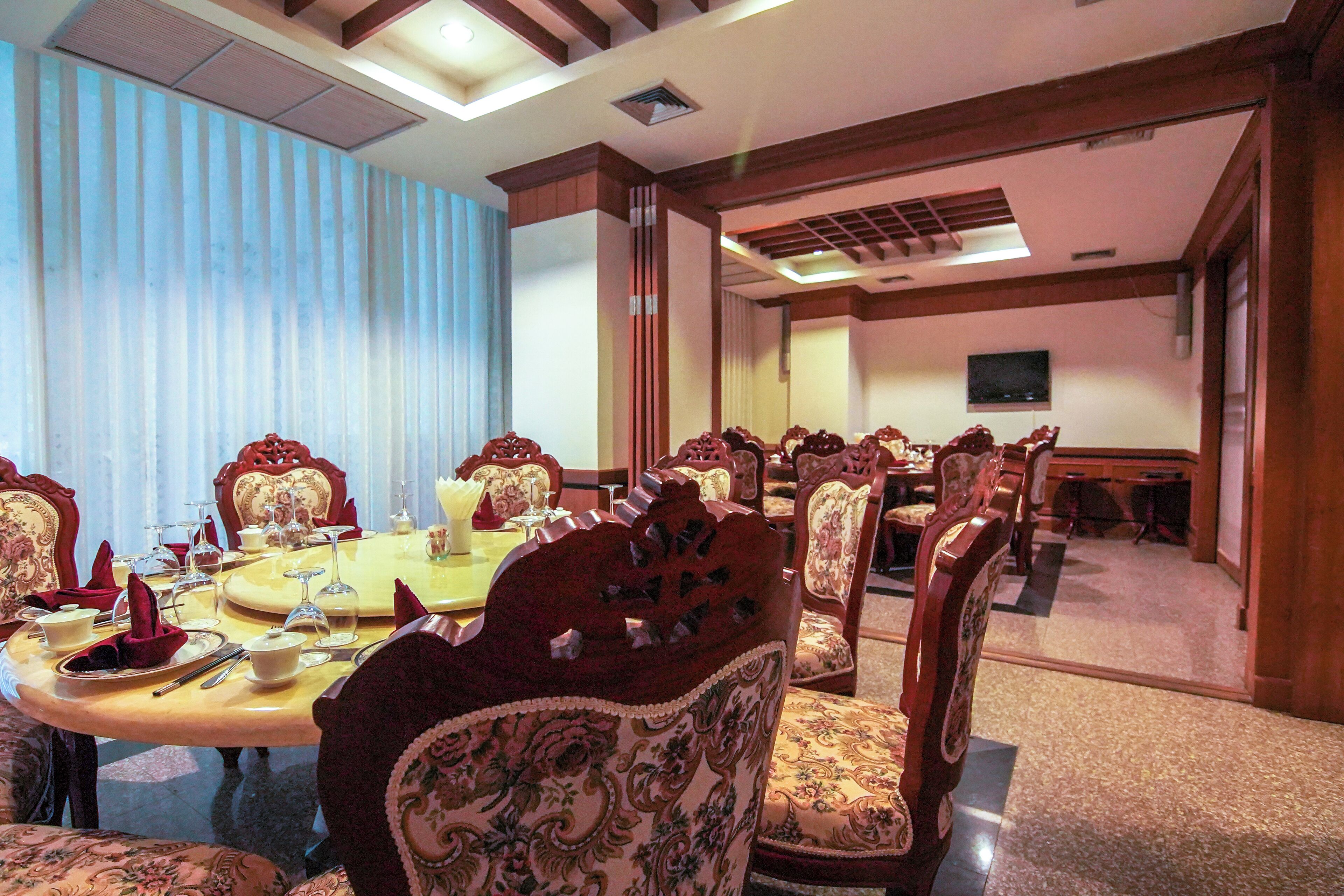 A formal dining room with a large oval table, ornate chairs, and a television on the wall.