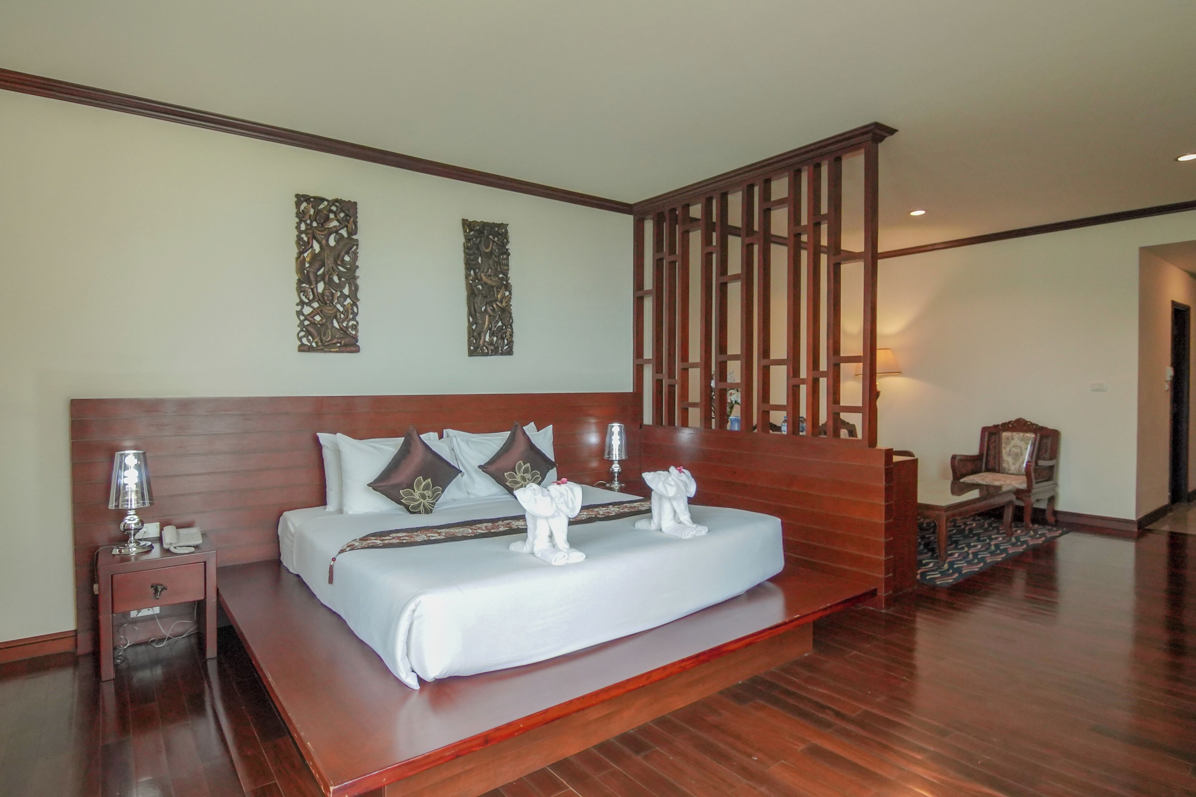 A spacious bedroom with a large bed, wooden headboard, decorative wall art, and a wooden partition.