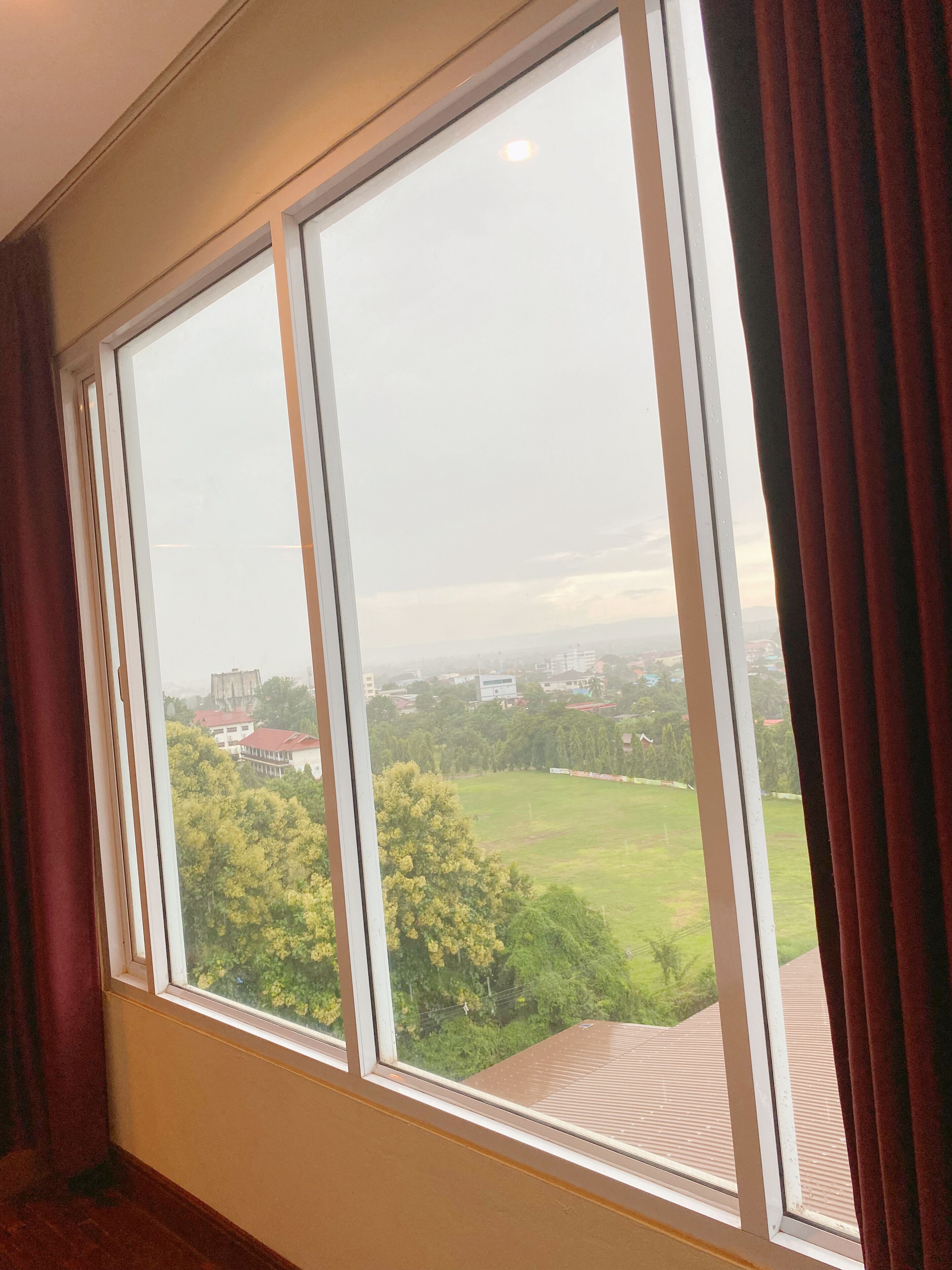 A room with a large window overlooking a green landscape and buildings.