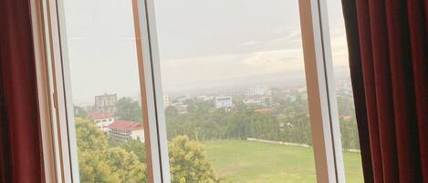 A room with a large window overlooking a green landscape and buildings.