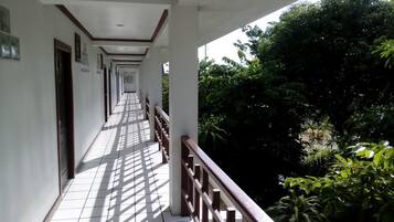 A long corridor with white tiled floors and wooden railings, leading to a lush green area with trees and plants.