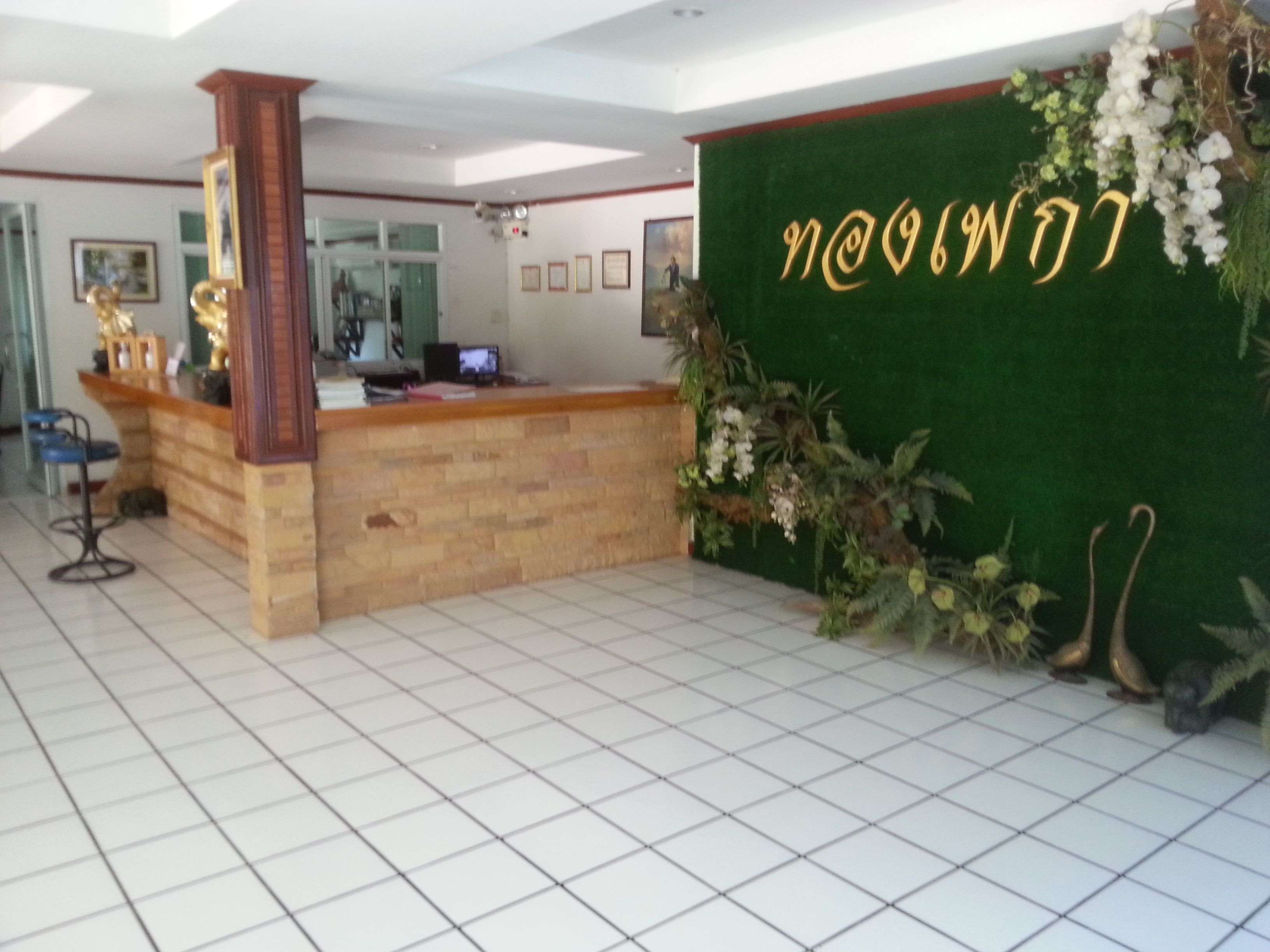 A reception area with a wooden counter, a green wall with gold lettering, and a tiled floor.