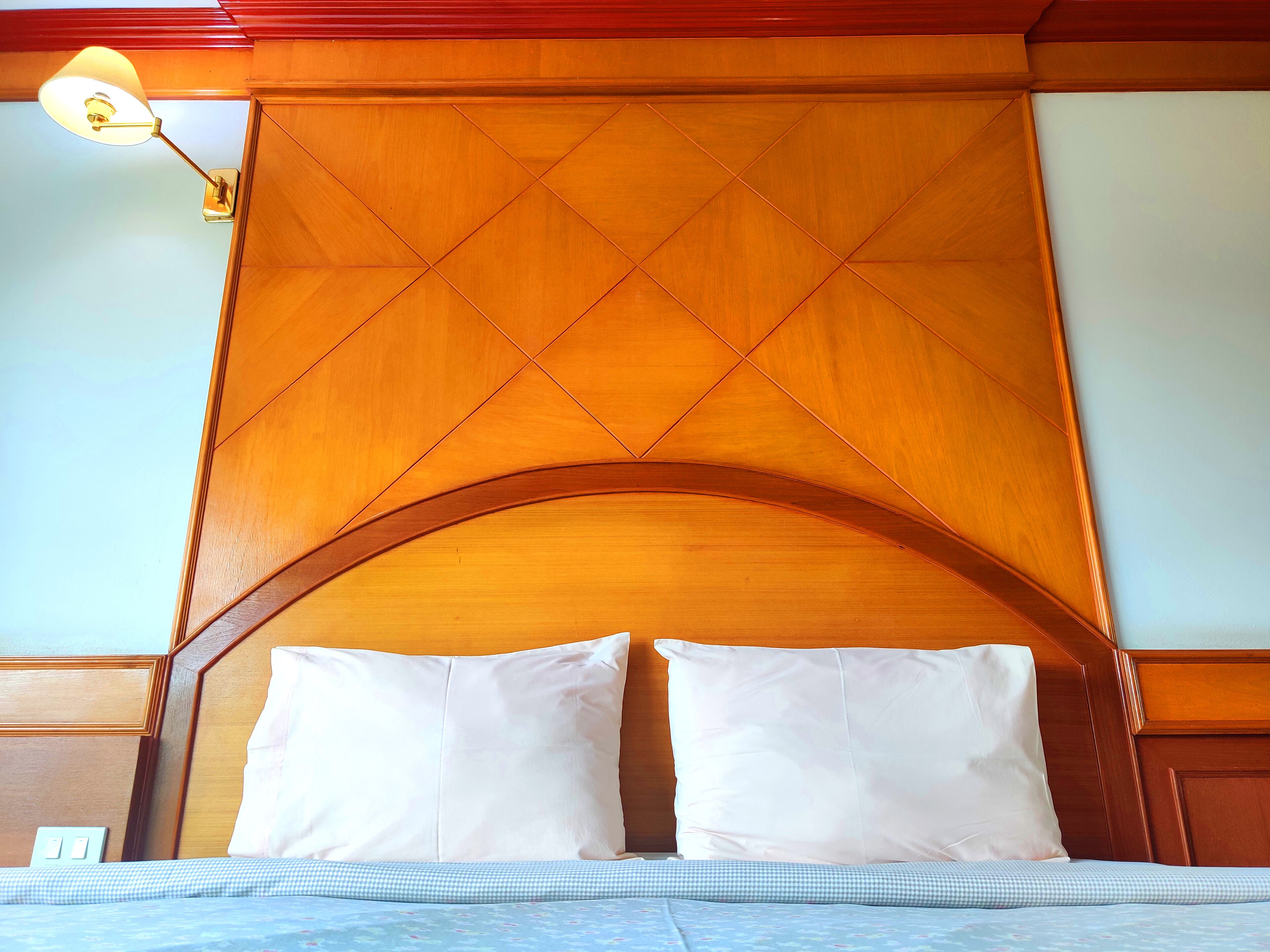 A hotel room with a wooden headboard, two white pillows, and a checkered bedspread.