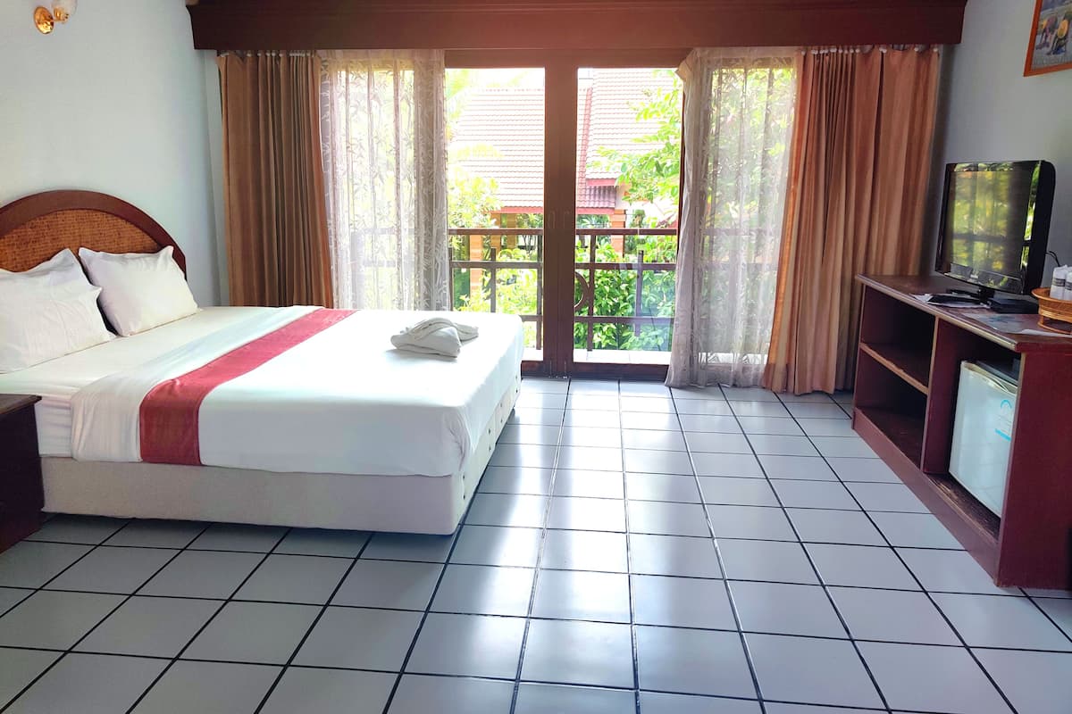 A hotel room with a bed, a television, and a balcony with curtains.