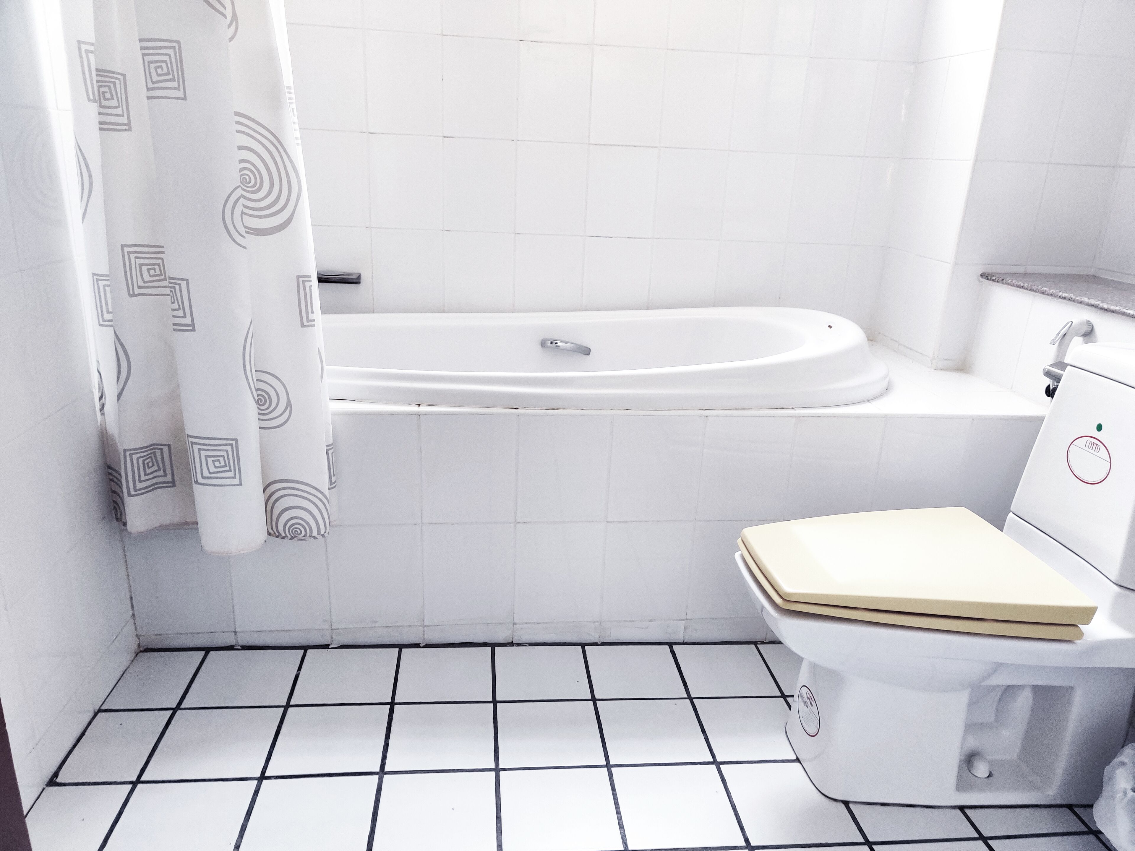 Un baño con una bañera blanca, un inodoro y una cortina de ducha con diseño geométrico.