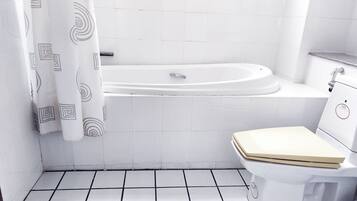 Un baño con una bañera blanca, un inodoro y una cortina de ducha con diseño geométrico.