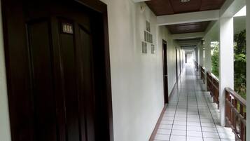 Un pasillo con puertas a un lado y una barandilla al otro, que conduce a una zona cubierta con suelo de baldosas.