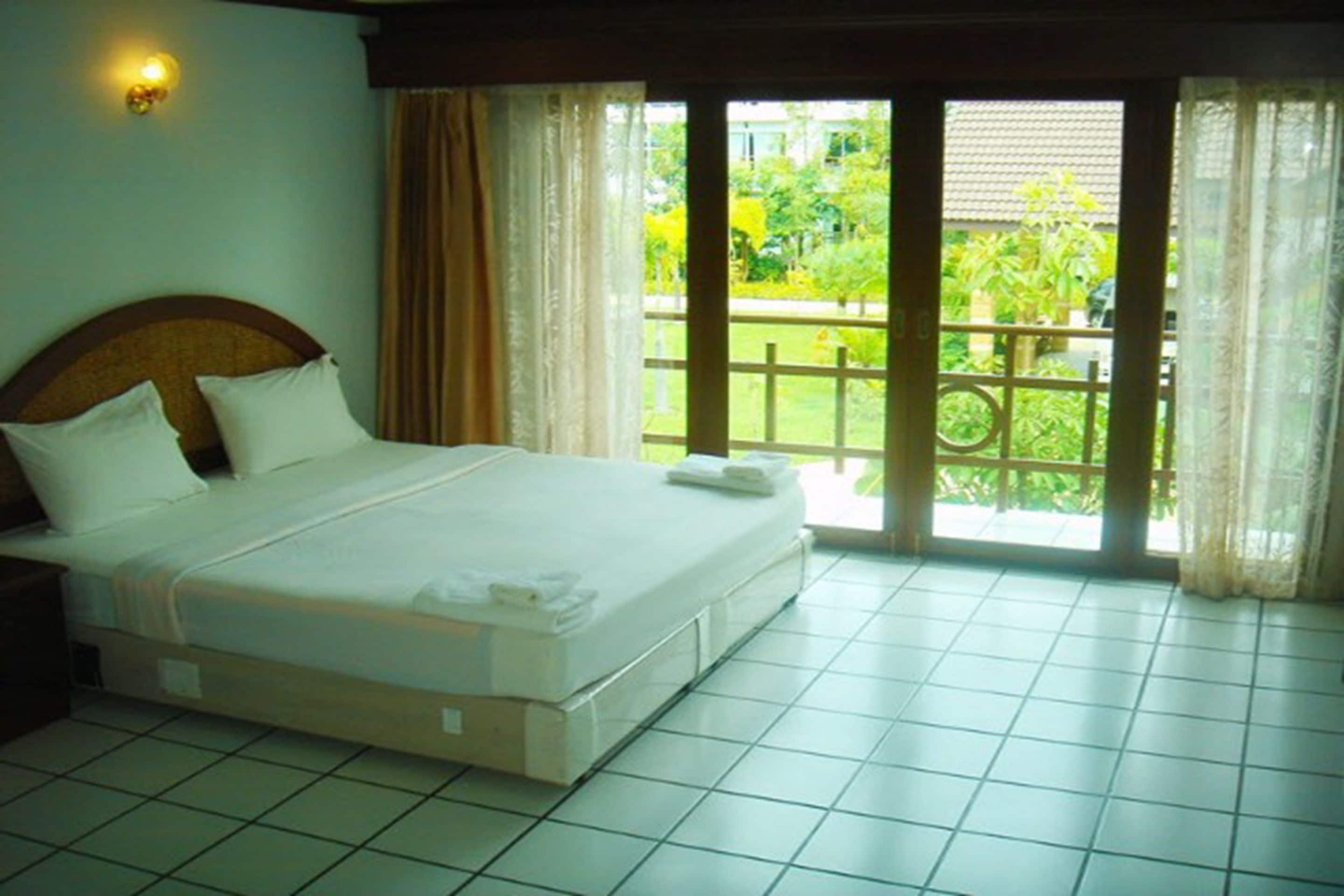 A hotel room with a bed, curtains, and a view of greenery outside.