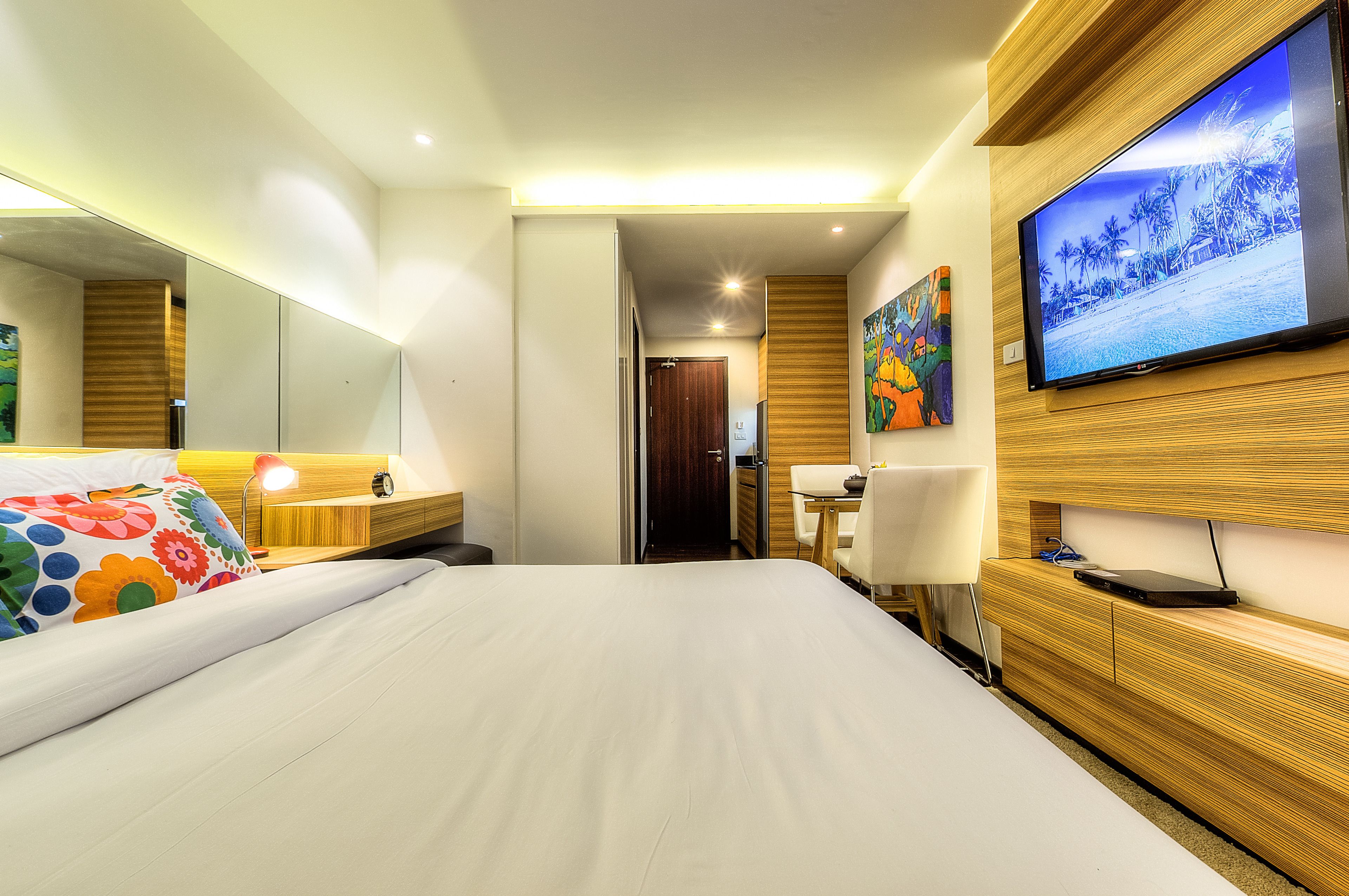 Ein Hotelzimmer mit einem großen Bett, einem Schreibtisch mit Stuhl, einem flachbildfernseher an der Wand und einer Wandverkleidung aus Holz.