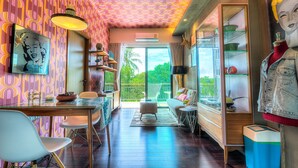 A room with a patterned wall, a dining area with chairs and a table, a sofa, and a large window with a view of greenery. - The Title Boutique Condotel (Rawai)