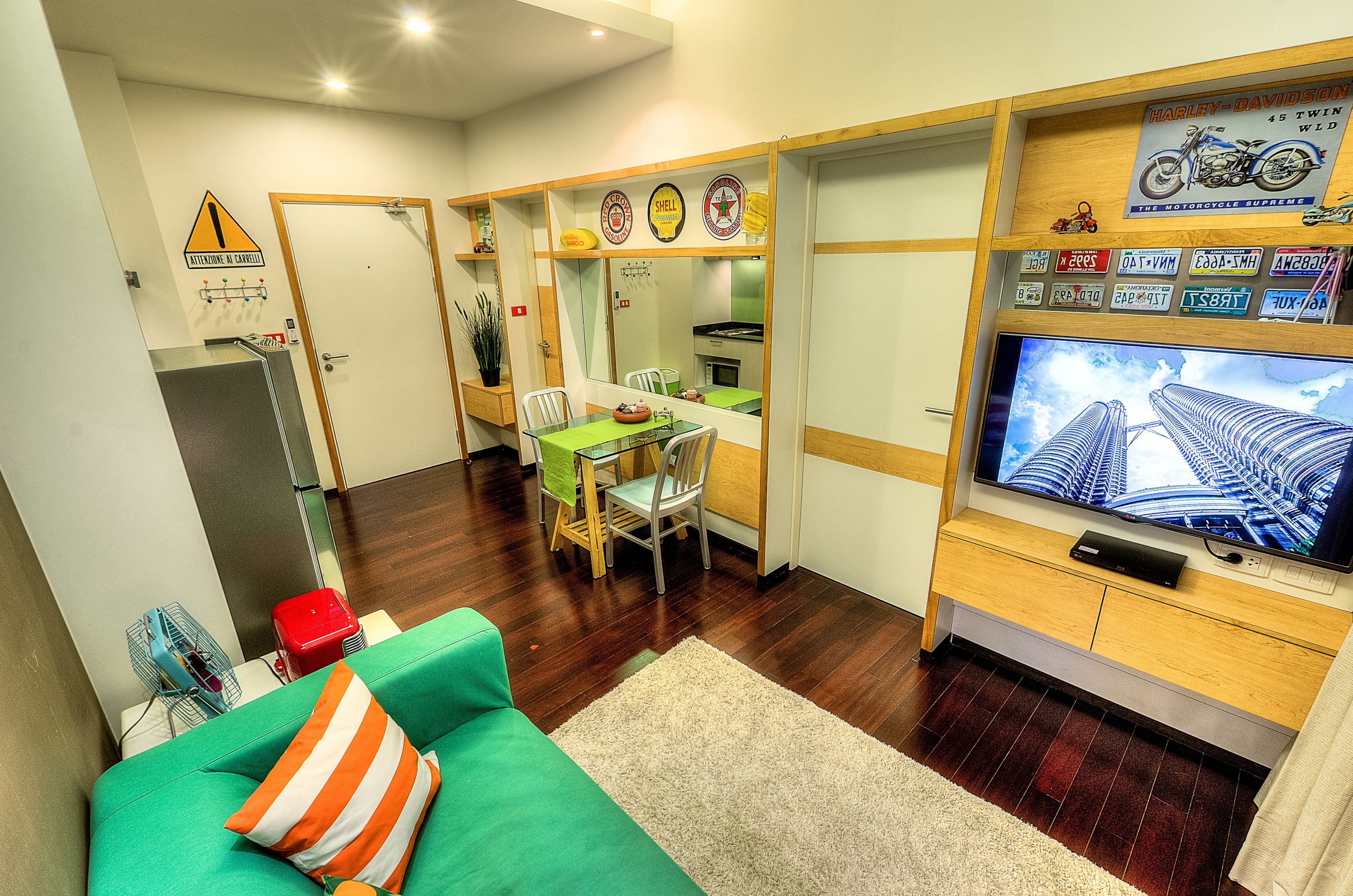 Un espace de vie compact comprenant un canapé vert, un coin repas avec des chaises, un coin cuisine et un téléviseur posé sur un meuble en bois.