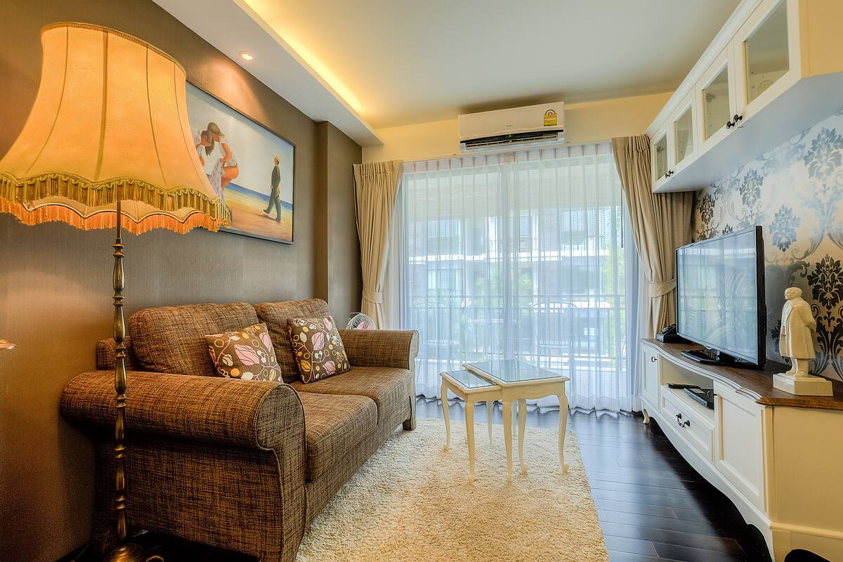 A living room with a sofa, a table, a lamp, a TV, and a window with curtains.