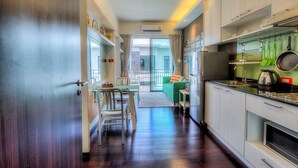 A modern kitchen with a dining area, a green sofa, and a view through a glass door. - The Title Boutique Condotel (Rawai)