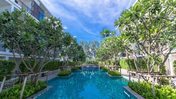 A swimming pool surrounded by lush greenery and modern buildings. - The Title Boutique Condotel (Rawai)