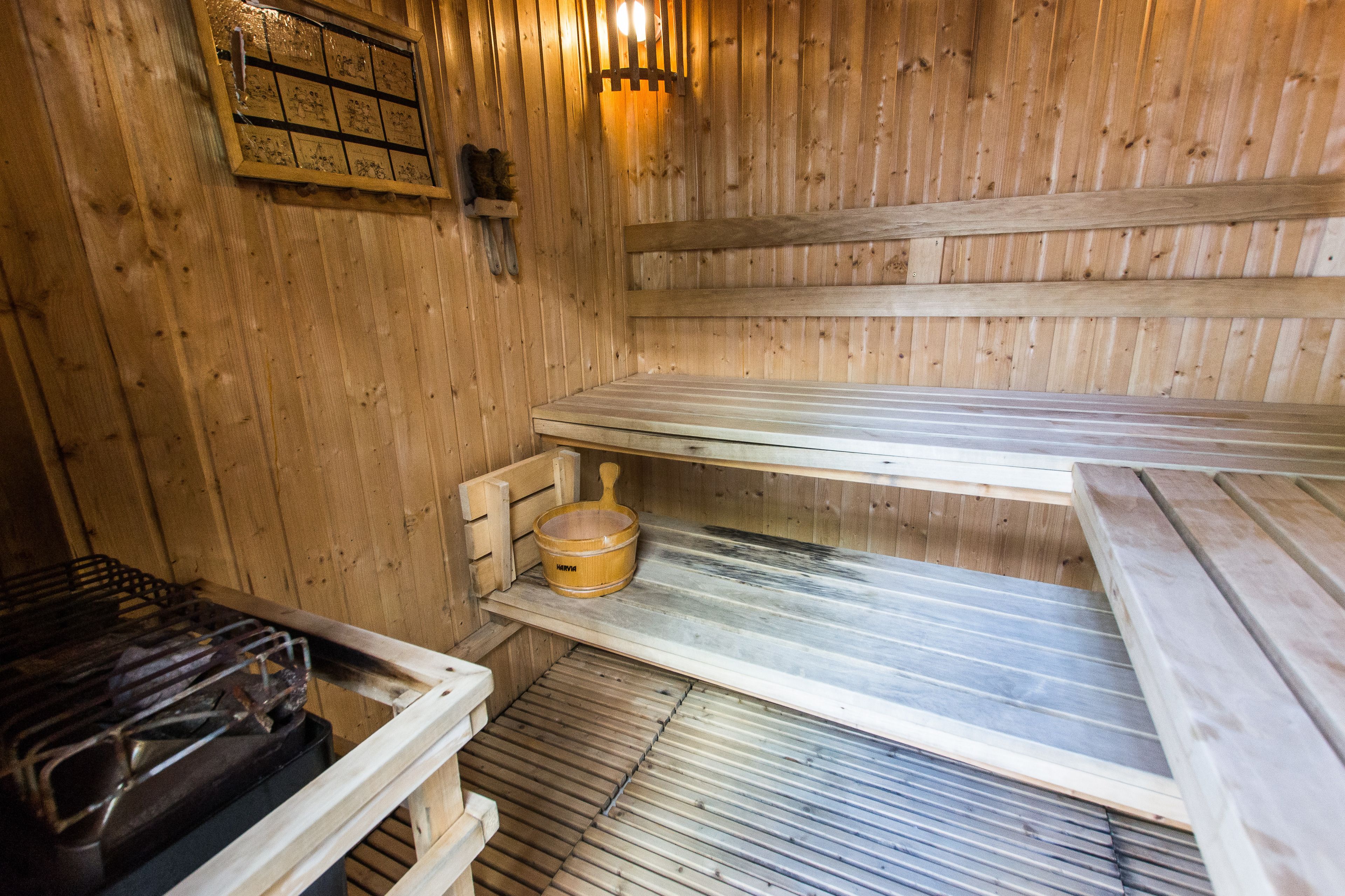A sauna with wooden walls and benches, a wooden bench on the floor, and a wooden bucket on a shelf.