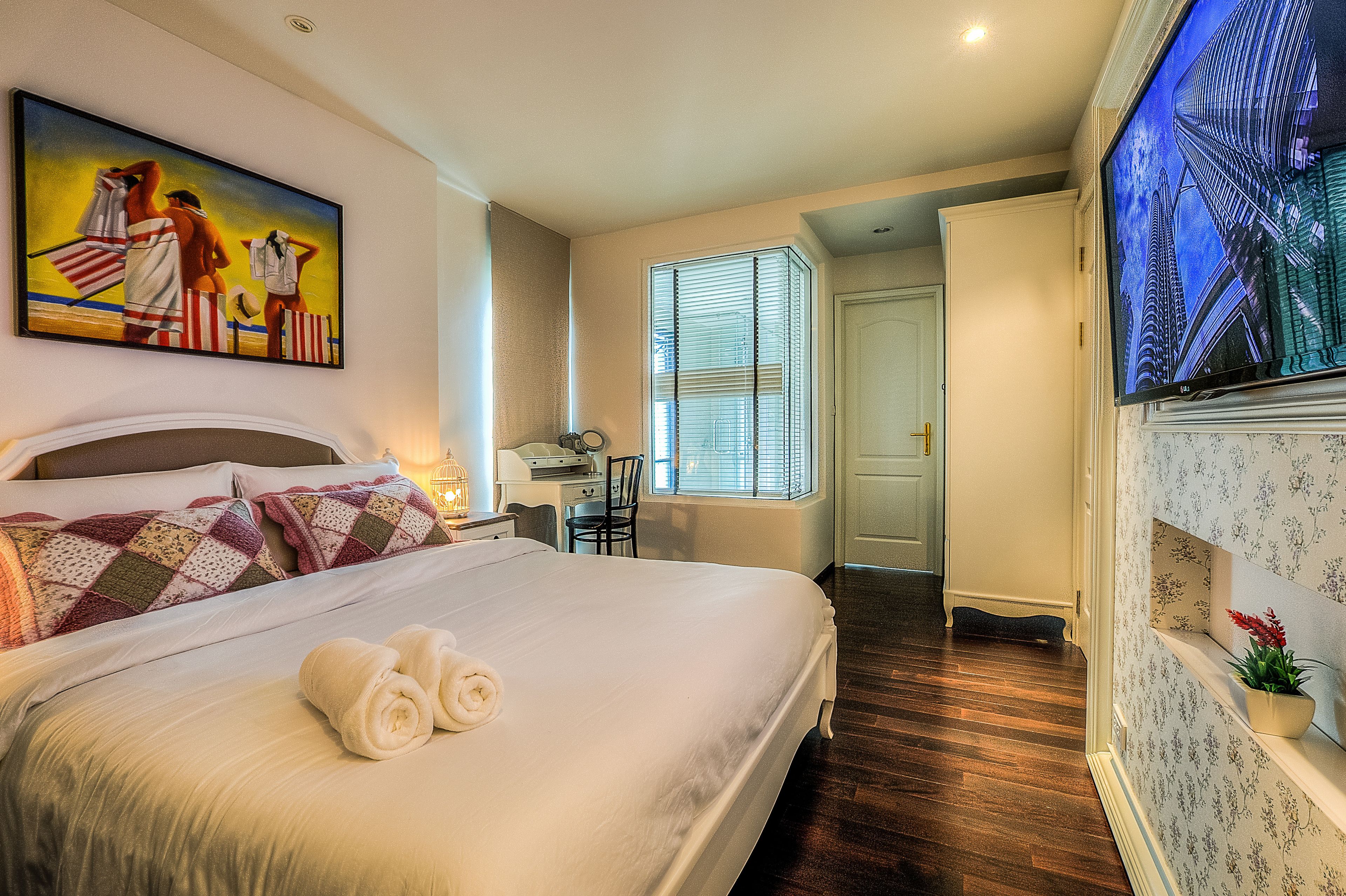 Una habitación de hotel con una cama grande, un escritorio, una silla, un televisor y una ventana con persianas.
