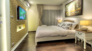A hotel room with a large bed, a TV mounted on the wall, a painting above the bed, and a nightstand with a lamp. - The Title Boutique Condotel (Rawai)