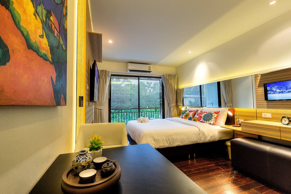 A hotel room with a bed, a TV, a desk, and a window with curtains.