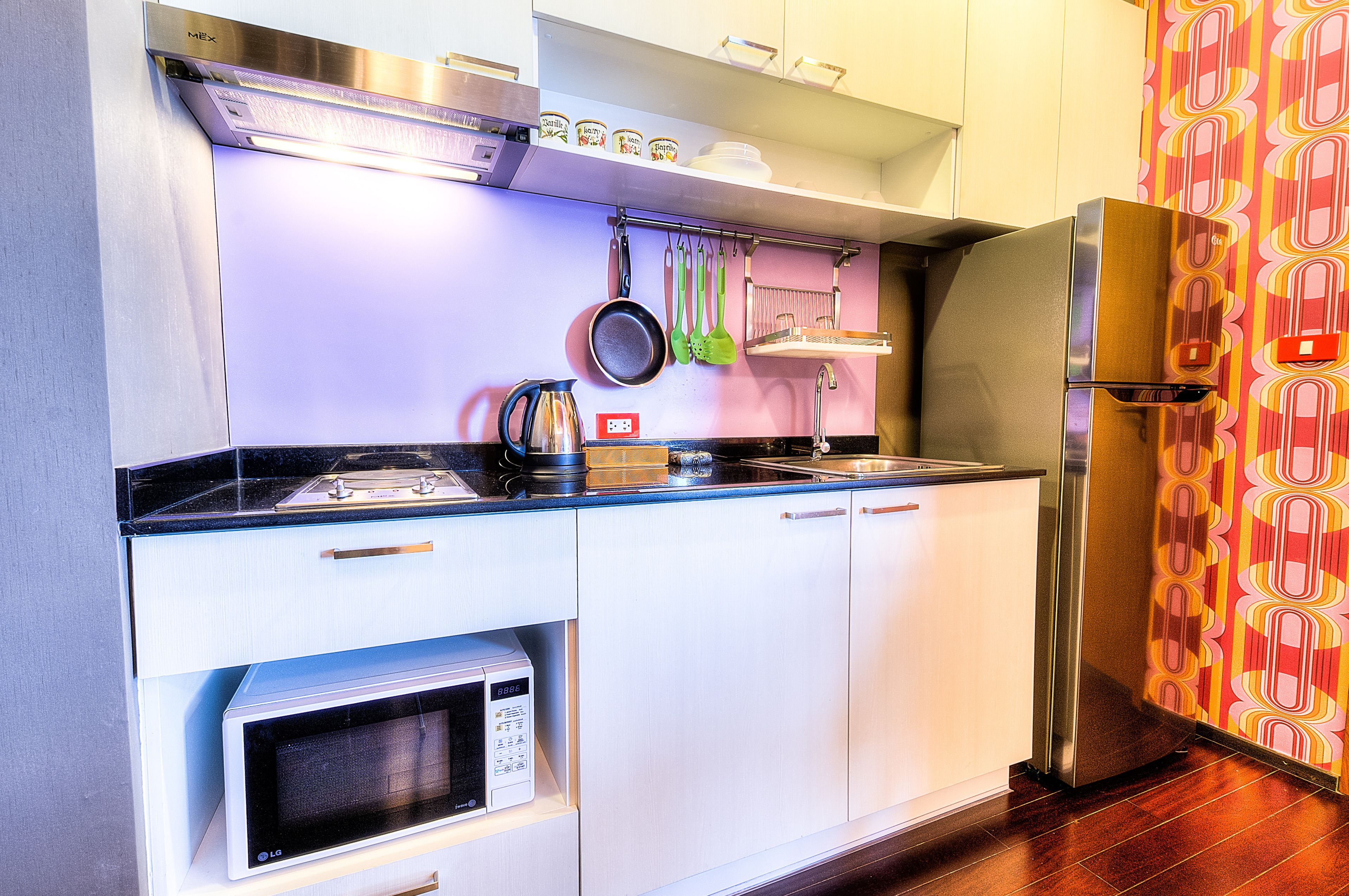 Une cuisine de taille réduite, dotée de meubles blancs, d’un réfrigérateur en acier inoxydable, d’un four à micro-ondes et d’une cuisinière à gaz.