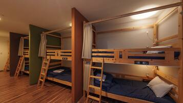 A dormitory room with bunk beds, wooden floors, and a ladder.