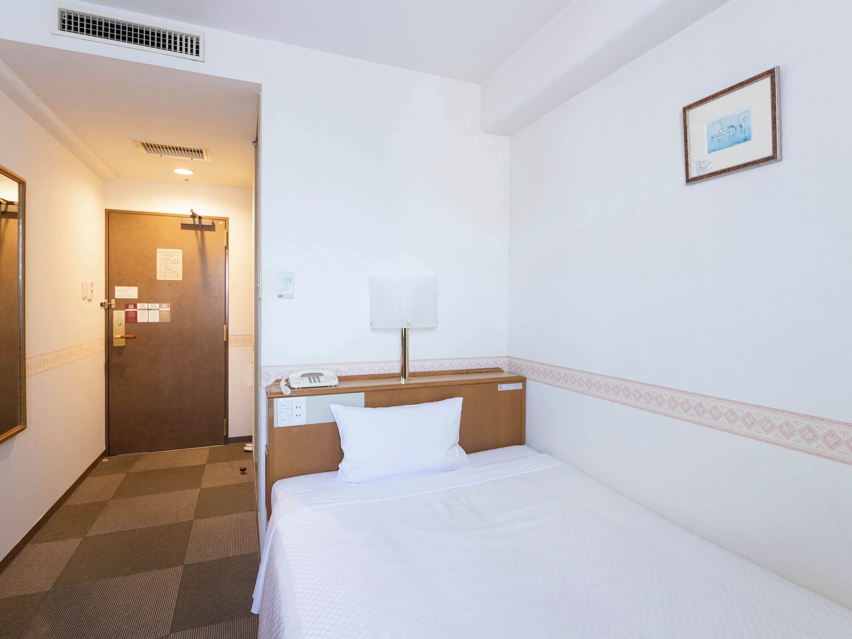 A hotel room with a bed, a bedside table with a lamp, a phone, and a door leading to another room.
