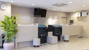 A hotel reception area with a modern design, including a reception desk, check-in kiosks, a clock, and a potted plant. - Hotel Wingport (Nagasaki)