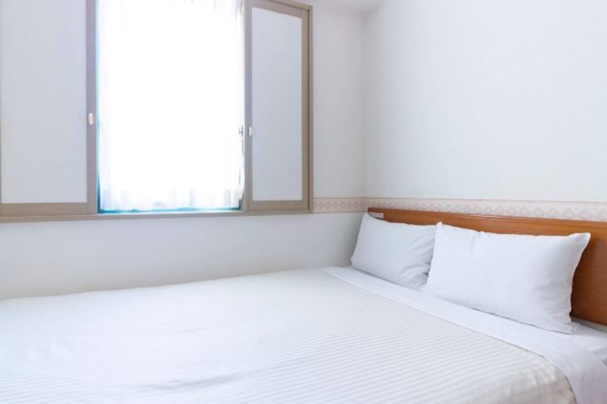 Una habitación de hotel con una cama individual, cabecera de madera y ventana con cortinas.
